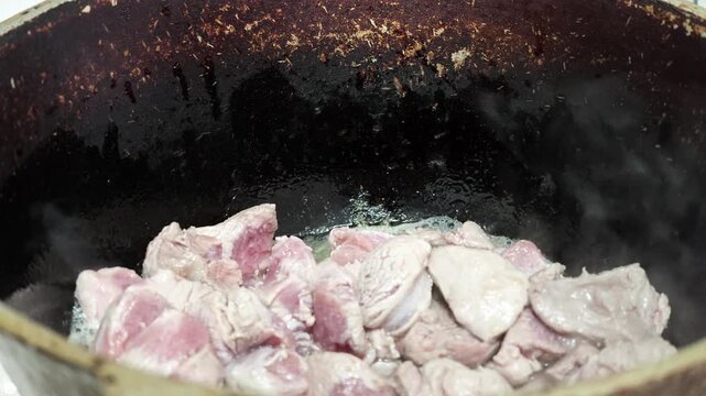 Close up scene shows irregular beef chunks browning in dark skillet with bubbling fat, rendered juices, pink centers, seared texture, and caramelized surfaces for rich home kitchen cooking action