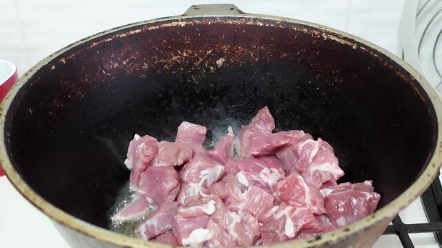 Close up scene shows irregular beef chunks browning in dark skillet with bubbling fat, rendered juices, pink centers, seared texture, and caramelized surfaces for rich home kitchen cooking action