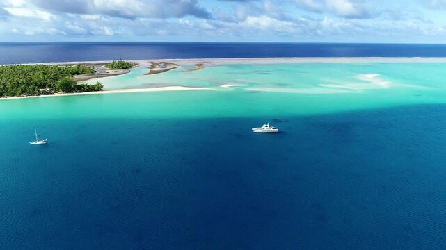 Sailboats anchor in the clear turquoise waters of a remote tropical lagoon.