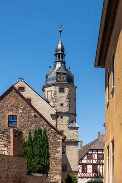 Historic Wettin Rathaus clock tower rises above stone houses and half-timbered homes under clear blue sky. Medieval townscape captures German heritage, masonry, rooftops, and quiet summer atmosphere