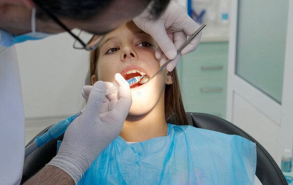 A pediatric dentist treats the teeth of a little girl sitting in the dental chair.