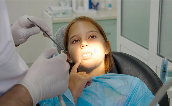 Pediatric dentist examining teeth of a brave girl sitting in dental chair