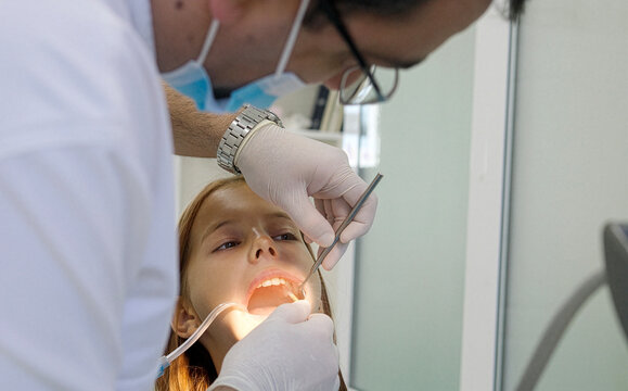 A pediatric dentist treats the teeth of a little girl sitting in the dental chair.