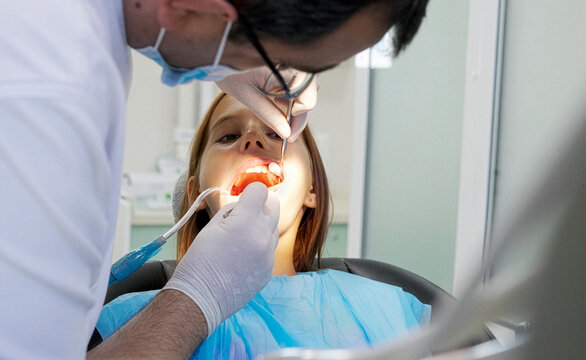 A pediatric dentist treats the teeth of a little girl sitting in the dental chair.