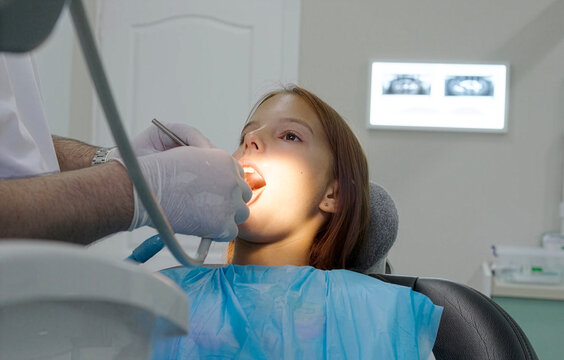 A pediatric dentist treats the teeth of a little girl sitting in the dental chair.