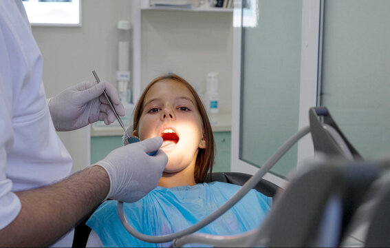 A pediatric dentist treats the teeth of a little girl sitting in the dental chair.