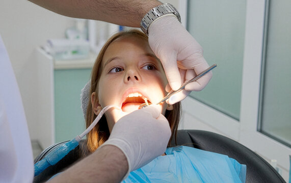 A pediatric dentist treats the teeth of a little girl sitting in the dental chair.
