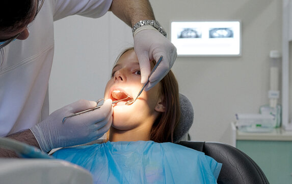 Pediatric dentist examining teeth with mirror and probe for young girl