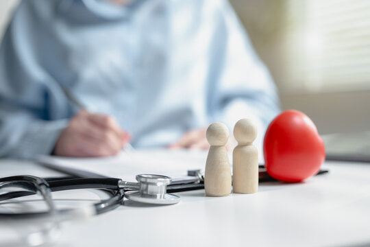 Wooden dolls with red rubber heart and medical stethoscope on insurance policy form table. Scene for family healthcare consulting, life coverage claim, and cardiac medical check up consultation.