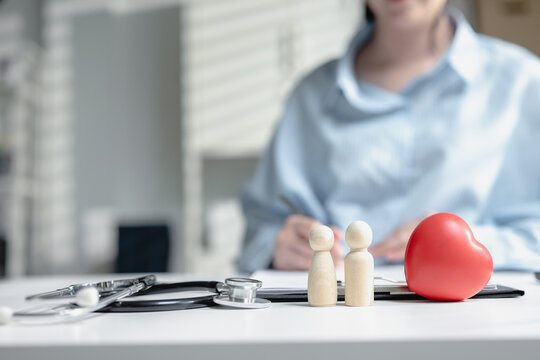 Wooden dolls with red rubber heart and medical stethoscope on insurance policy form table. Scene for family healthcare consulting, life coverage claim, and cardiac medical check up consultation.