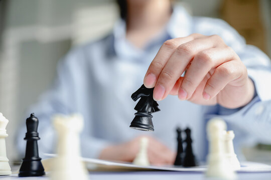 Close up hand of businesswoman moving black knight chess piece on desk for corporate strategy planning and leadership management in office. Concept of business success and tactic under pressure.