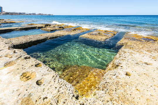 Wide-angle view of the historic Roman Baths in Sliema, Malta, featuring natural limestone bathing pools and crystal-clear Mediterranean waters along the island's picturesque coastline.