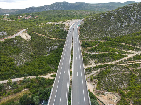 Vehicles moving on a high motorway bridge, aerial drone view. Traffic on a modern highway viaduct. Transportation on an elevated dual-carriageway.