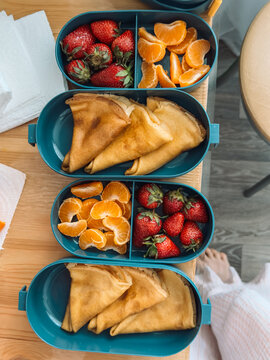 Healthy homemade lunch boxes with pancakes, strawberries and orange slices on table.