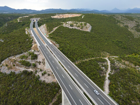 Tunnels in front of high motorway bridge, aerial drone view. Traffic on a modern highway viaduct. Transportation on an elevated dual-carriageway.