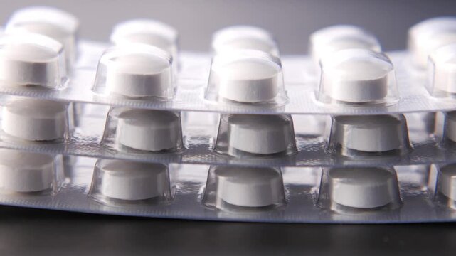 Three stacked blister packs of white pills rotating on dark background close up footage