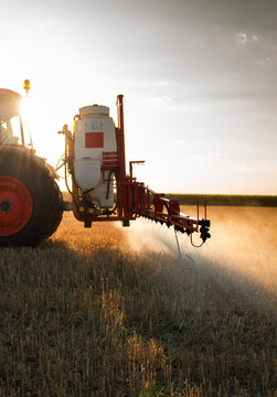 Tractor spraying harvested wheat stubble field at sunset