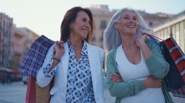Two happy and stylish senior women friends enjoying their time together. Laughing and smiling heartily while standing against a brick wall. Showcasing a concept of lasting friendship and joy in aging