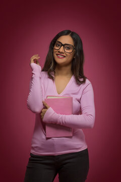 Portrait of a smiling young teenager wearing spectacles holding a book