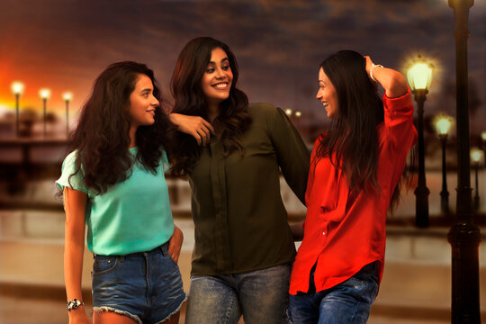 Three girl friends standing outdoors in evening and talking