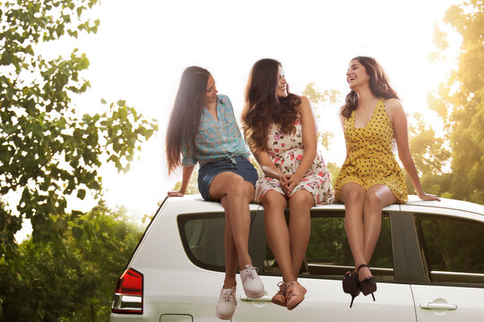 Three girl friends sitting on top of a car and talking