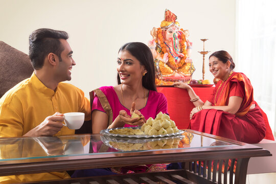 Husband wife sitting together while wife makes modaks and mother and law watches