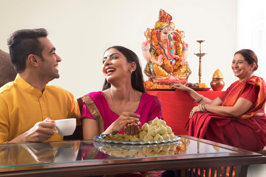 Husband wife sitting together while wife makes modaks and mother and law watches