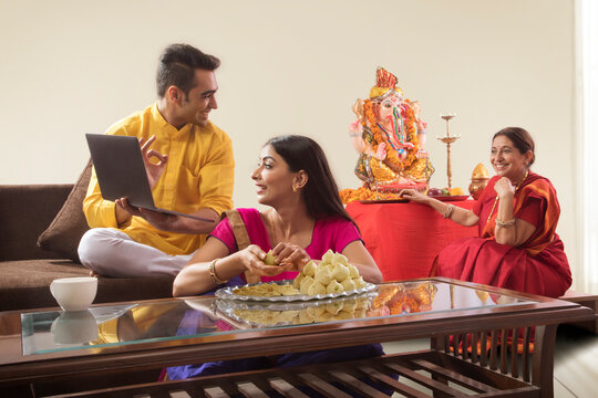 Husband wife sitting together while wife makes modaks and husband showing his mother laptop