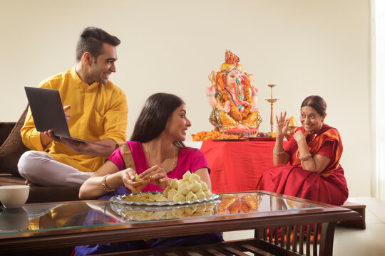Husband wife sitting together while wife makes modaks and husband showing his mother laptop