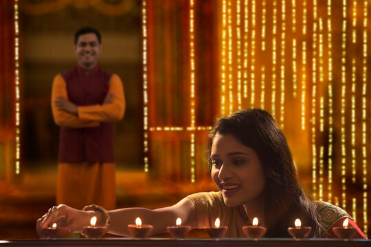 Woman decorating the house with diya on the occasion of diwali with husband standing in background