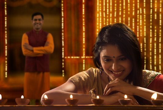 Woman decorating the house with diya on the occasion of diwali with husband standing in background