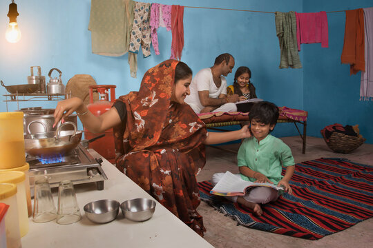 Childs studying in the kitchen while his mother is cooking