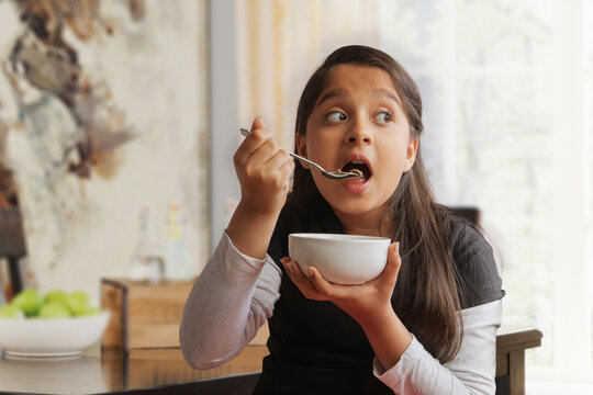 Girl eating breakfast in a bowl sitting at dining table looking away