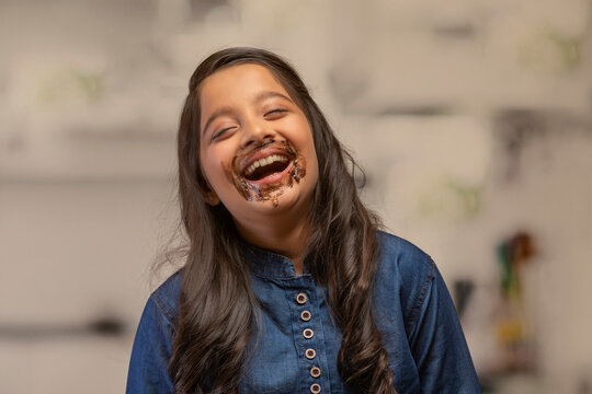 Girl with chocolate marks around her mouth laughing with eyes closed