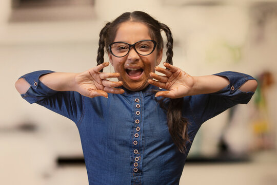 Girl in eyeglasses with chocolate marks around her mouth and on hands laughing in joy
