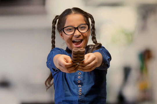 Happy girl in eyeglasses offering a chocolate bar holding it with both hands