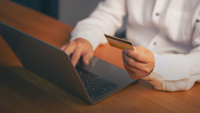 Asian man using a laptop and credit card for online shopping and secure payment. This e-commerce technology allows quick internet business transactions, digital buying, and mobile banking.