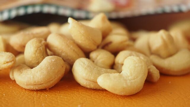 Close up shot of roasted cashew nuts scattered on an orange surface with a subtle tilt shift effect