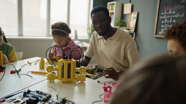 Multiethnic children assembling robotics kits in classroom with African American male teacher providing guidance. Footage is ideal for promoting STEM education and modern school programs