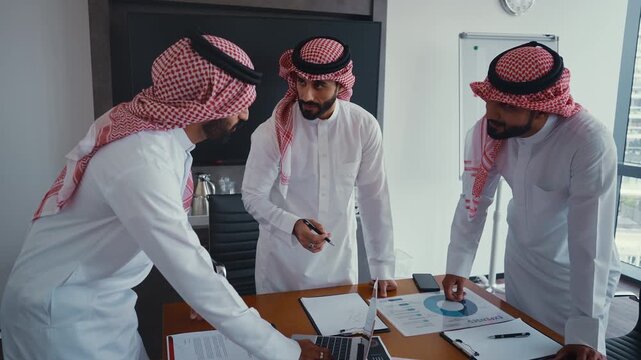 Arab businessmen wearing emirati kandura meeting in office for business deal - Corporate business group of middle-eastern people working in an international company in middle east