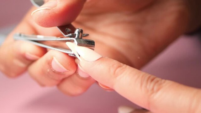 A close-up shot of a woman carefully cutting her long, pointed artificial nails with a silver nail clipper in a bright and well-lit setting