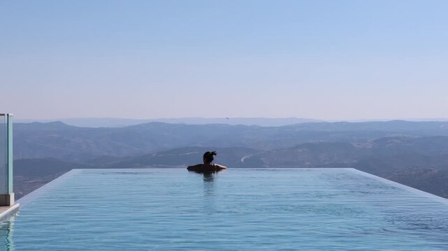 Woman relaxing in infinity pool enjoying mountain view