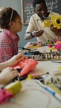 Vertical video of African American male teacher explaining robotics toy to multiethnic children in classroom. Clip is ideal for promoting STEM education and modern school technology programs