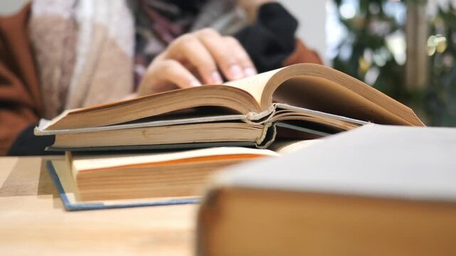 Person wearing hijab reading stack of old books on wooden table dynamic footage