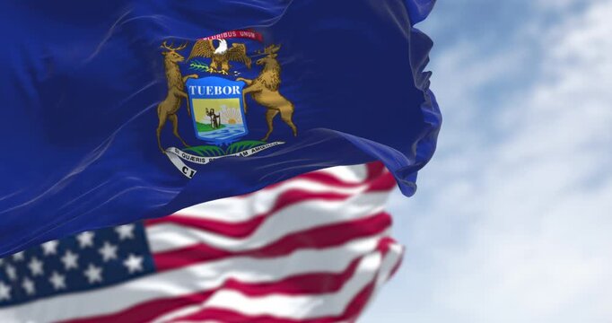 Michigan state flag and national american flag waving in the wind on a clear day