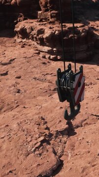 A cable system is set up on rocky ground. The pully hangs down, ready to help lift weight. Surrounding rocks show a dry environment. The scene indicates a work site or construction area.