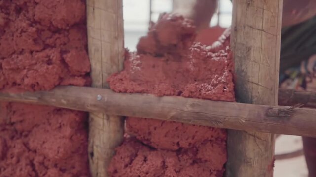Person building wattle and daub wall with raw earth material. Sustainable building practice using wattle and daub technique