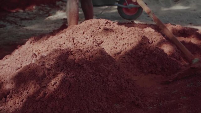 Brazilian worker mixing red clay and sand with a hoe. Traditional building technique for sustainable housing, also known as wattle and daub
