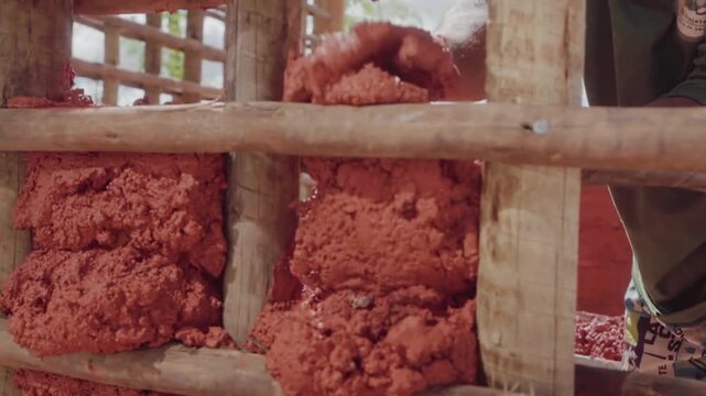 Close up of a worker's hand pressing raw earth into a wooden lattice. Sustainable building practice using wattle and daub technique