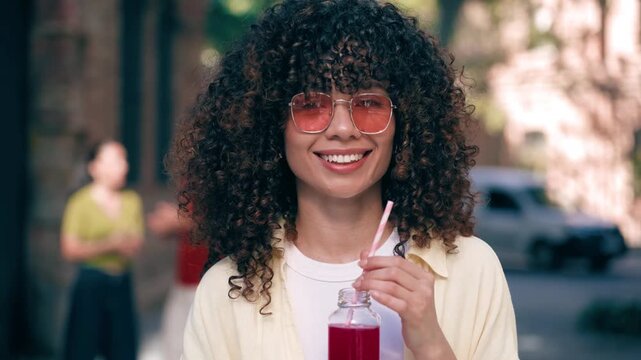 Video of beautiful woman drinking red juice while smiling at camera in the street.